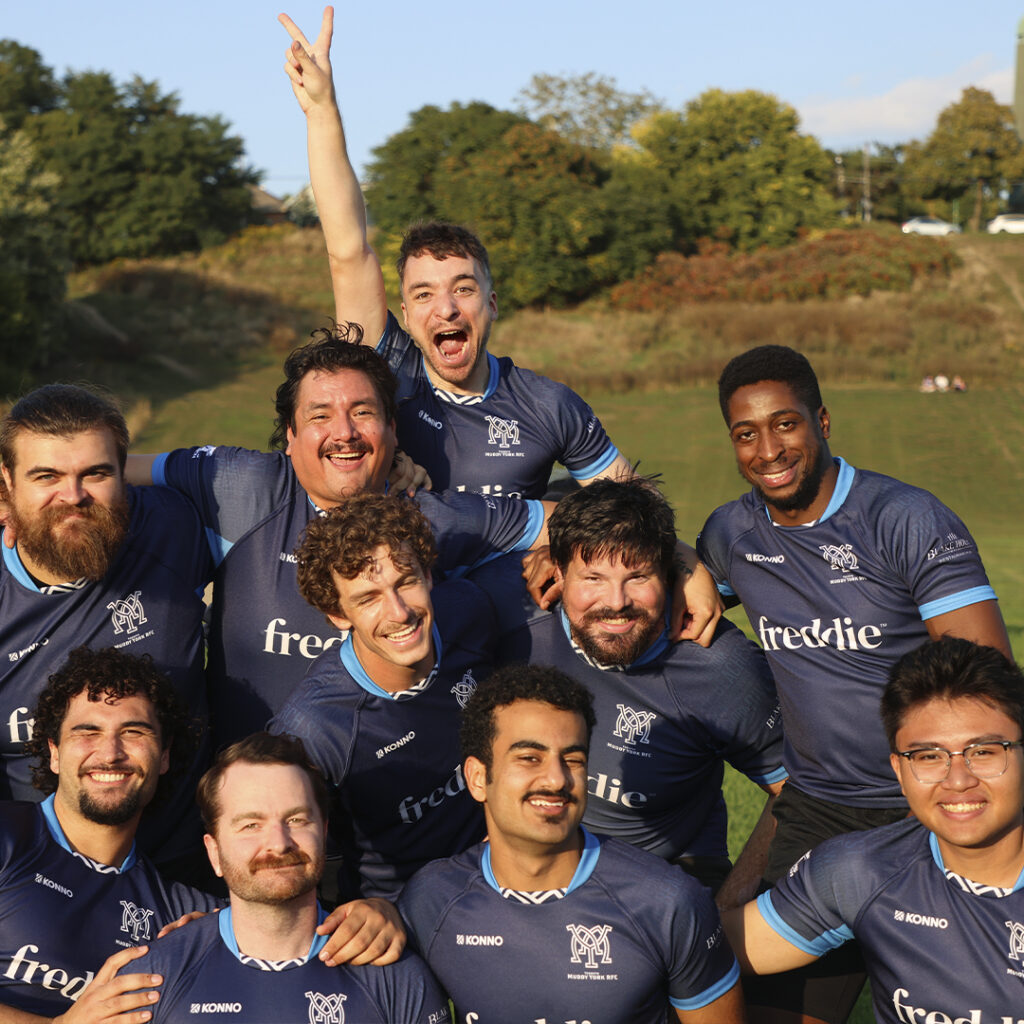 Muddy York's Men's + team posing and laughing for a goofy photo in their navy jerseys.